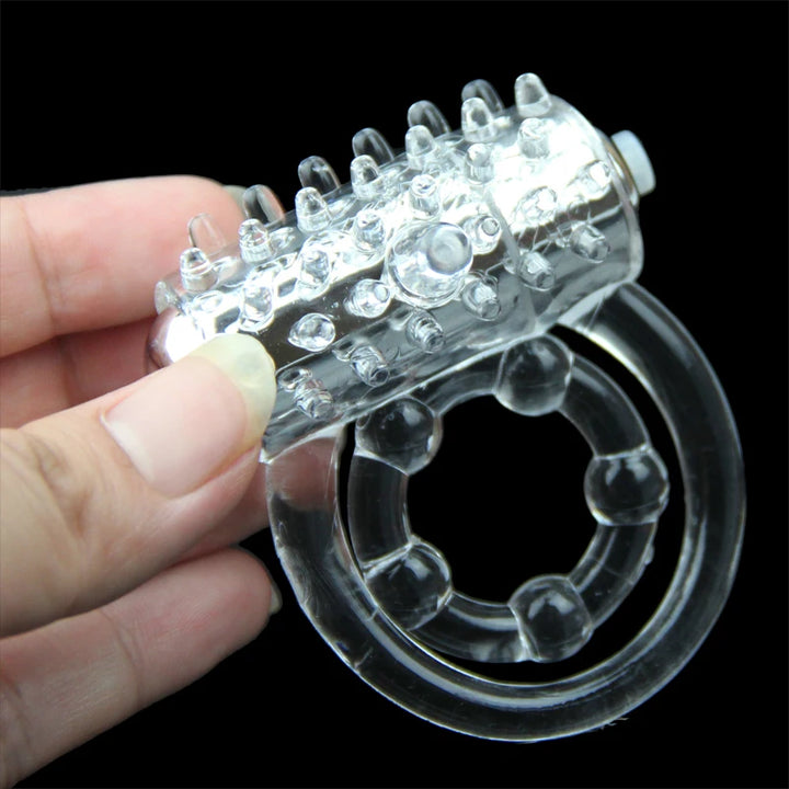 A clear transparent cock ring with a vibrator being held by a person on a black background