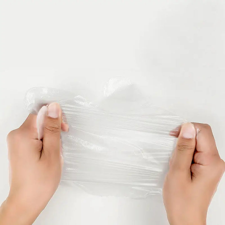 Two hands pulling a disposable clear plastic glove at the sides to show that it stretches but doesn't rip