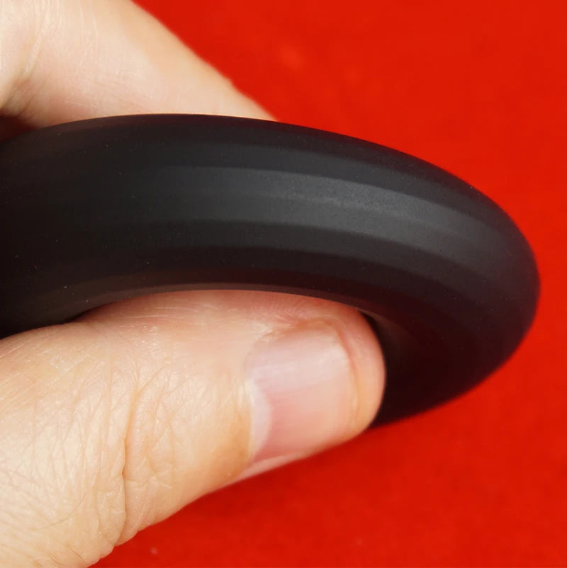 Black silicone rubber penis constriction band held between fingers against a red background