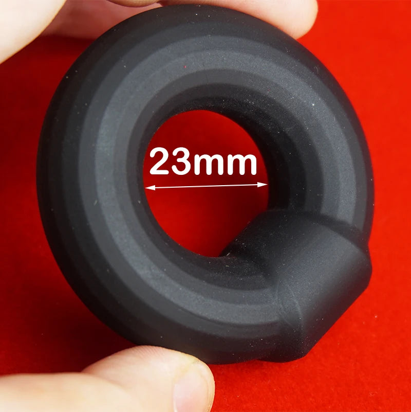 Black silicone rubber cock ring with '23mm' interior dimensions label held against a red background