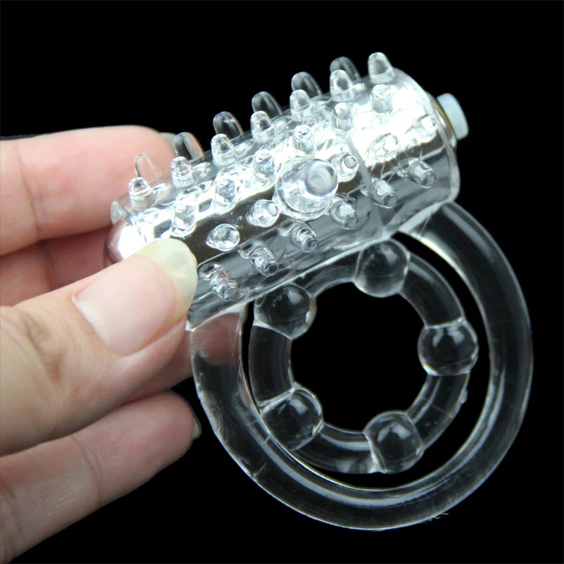 A clear transparent cock ring with a vibrator being held by a person on a black background
