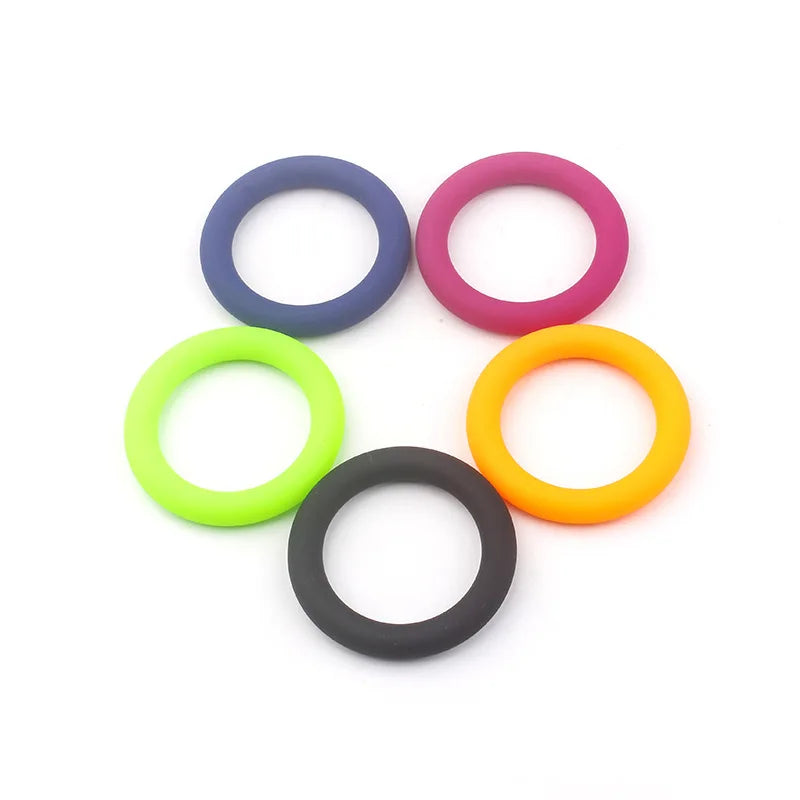 This photo shows five color coded cock rings, one of each of the five colors of black, blue, magenta, lime green, and tangerine orange